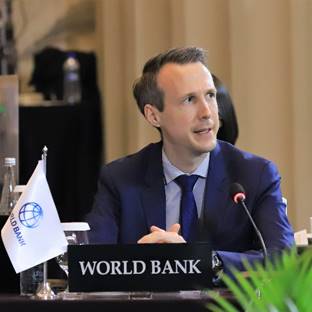 A person in a suit sitting at a podium
Description automatically generated